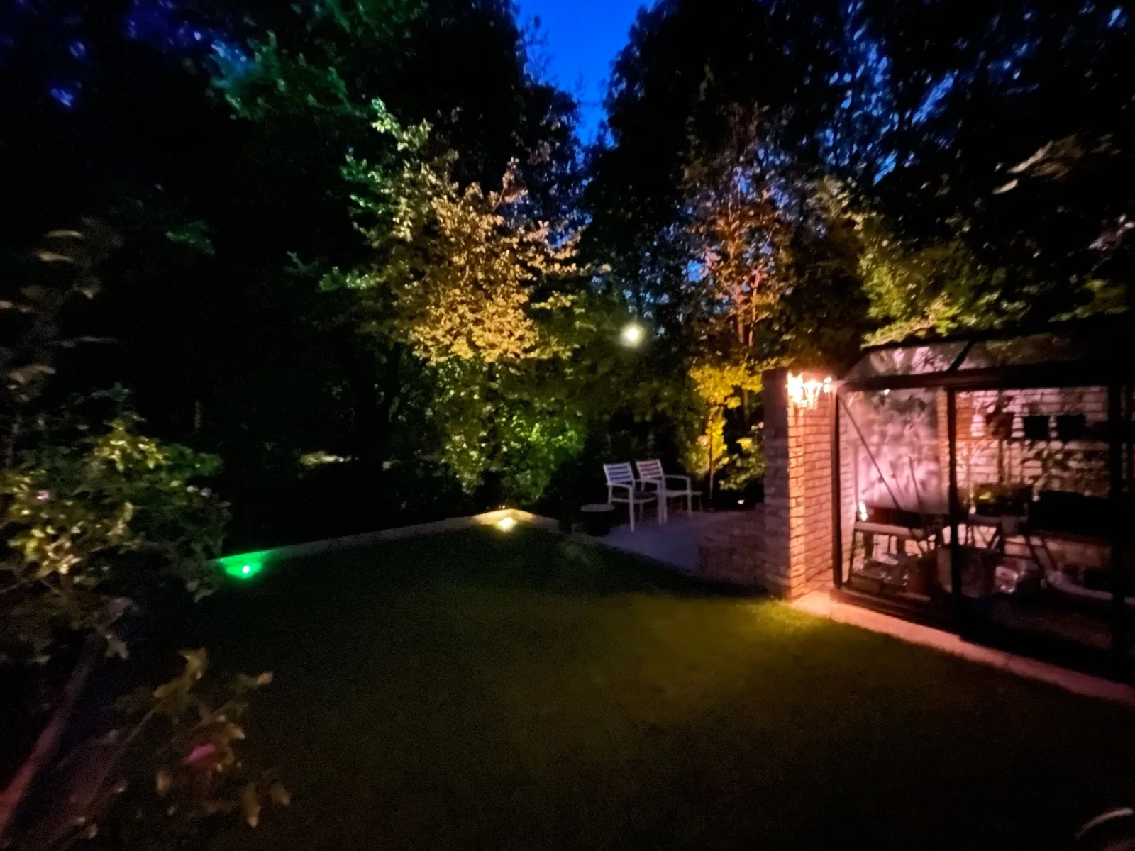 Donkere tuin met verlichting en zitgedeelte.