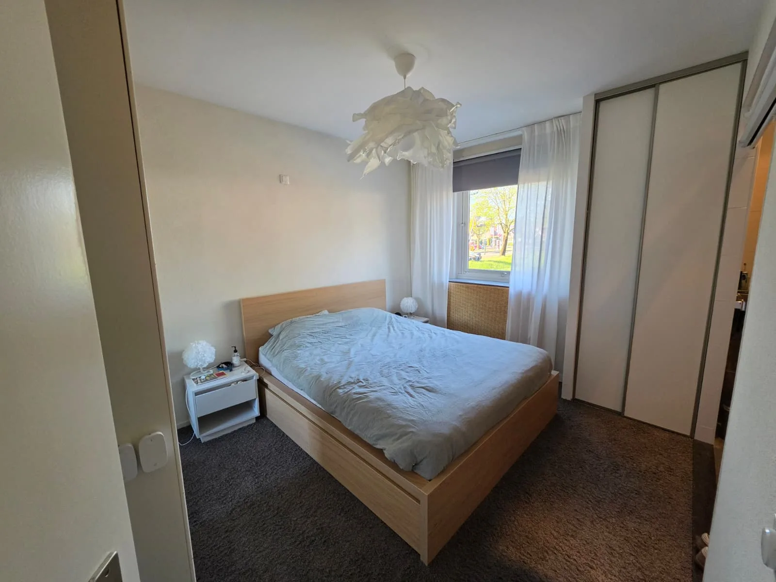Slaapkamer met bed, gordijnen en kast in appartement.