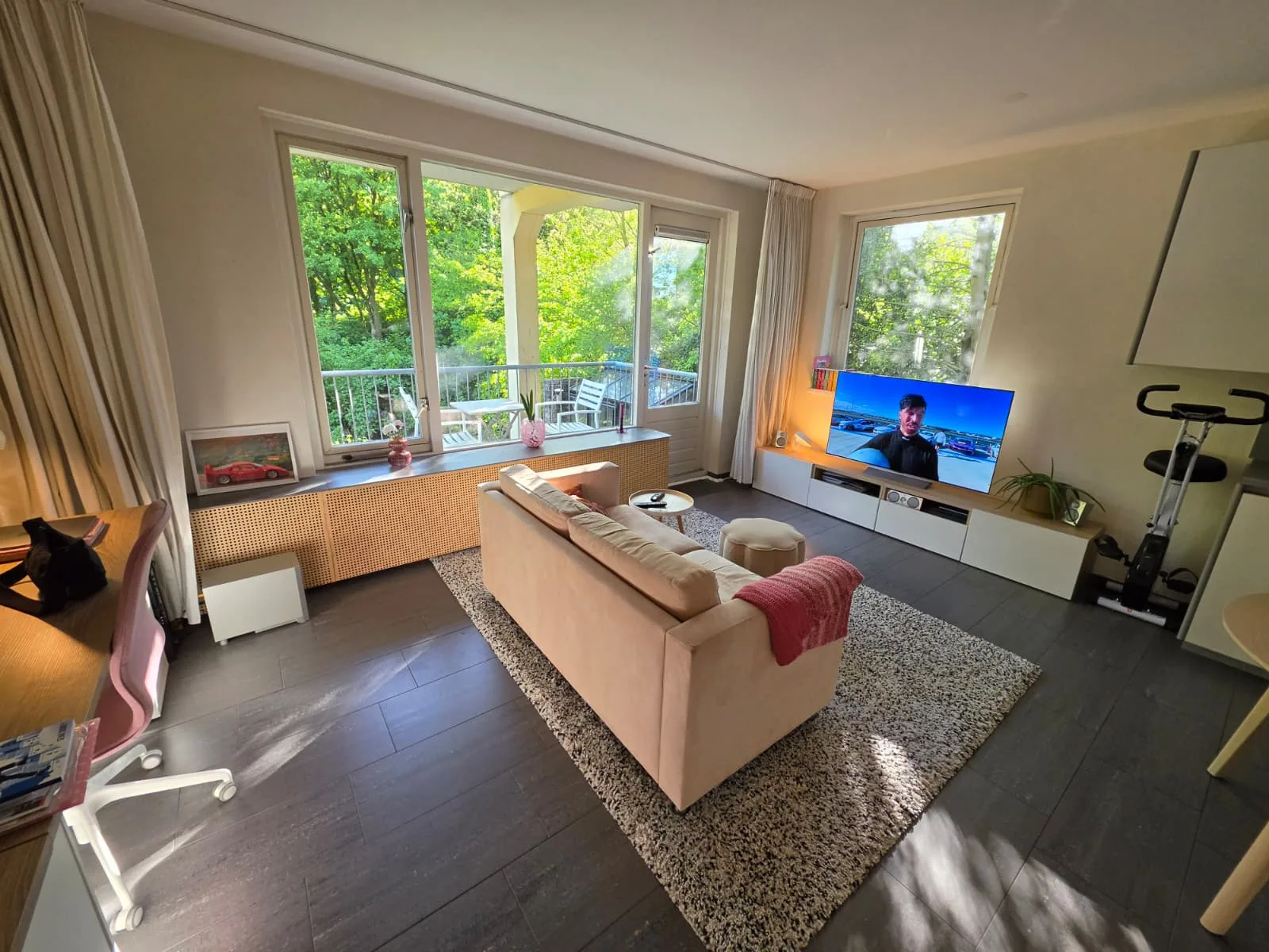Lichte woonkamer met bank, tv en uitzicht op groen.